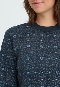 Sweatshirt marine avec un motif géométrique en bleu clair. Col côtelé, texture douce et manches longues avec une coupe ajustée.
