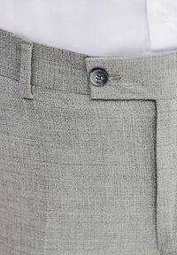 Szare spodnie z materiału mają teksturowaną strukturę, gładki przód oraz pojedyncze zapięcie na czarny guzik w talii. Widoczny detal przeszycia.