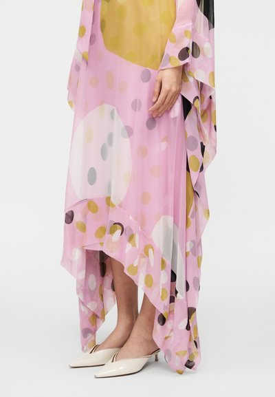 Voľné ružové šaty s veľkými farebnými bodkami, nosené s krémovými mulemi na nízkom opätku s ostrou špičkou.
