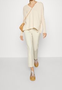 Pull beige en maille avec col en V et fentes latérales, associé à un pantalon ajusté couleur crème clair. Chaussures avec semelle épaisse et design à lacets.