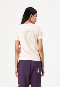 Ljusrosa bomulls t-shirt med en färgglad blommig grafik med en kameleont och ordet "CONVERSE" på baksidan. Korta ärmar, rund halsringning.