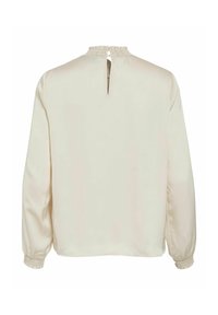 Blusa crema de manga larga, con puños fruncidos y una abertura en la parte trasera en forma de lágrima. Tela suave y ligera con un brillo mínimo.