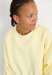 Felpa gialla Nike con scollo rotondo e vestibilità oversize, caratterizzata da un piccolo logo bianco sul petto. Tessuto liscio e morbido.