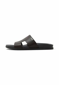 Sort slidesandal med bred læderrem med udsk�åren design og flad sål, mærket med et lille metalbrandmærke.
