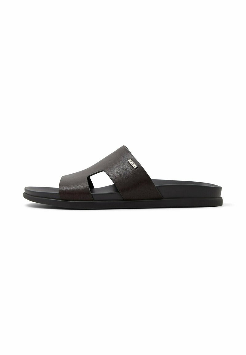 Sort slidesandal med bred læderrem med udskåren design og flad sål, mærket med et lille metalbrandmærke.