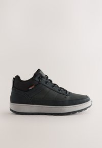 Schwarzer High-Top-Sneaker mit grauer Sohle, Schnürung vorne, grobem Profil und Cordura-Gewebe-Etikett auf beigem Hintergrund.