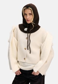 Sweter z mieszanki wełny w kremowym kolorze z oversize'owymi rękawami, zestawiony z ciemnobrązową prążkowaną bluzą z kapturem z sznurkami i metką z logo.