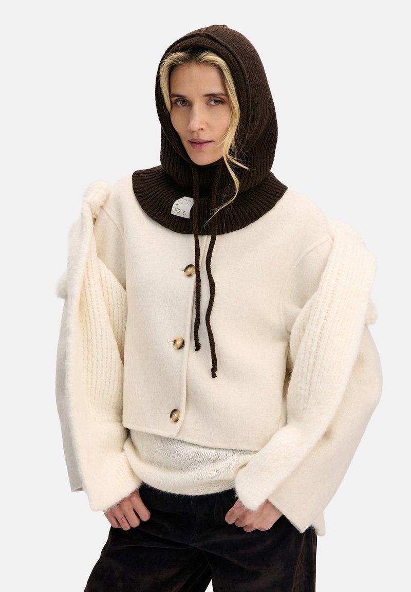 Sweter z mieszanki wełny w kremowym kolorze z oversize'owymi rękawami, zestawiony z ciemnobrązową prążkowaną bluzą z kapturem z sznurkami i metką z logo.