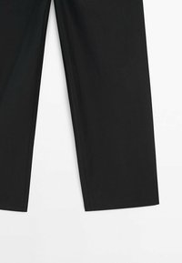 Pantalon noir à jambes droites avec coutures marquées sur fond blanc, montrant la moitié inférieure de la cuisse à l'ourlet.