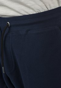 Jogging en bleu marine fabriqué en tissu texturé, avec une taille élastique dotée d'un cordon de serrage et des poches latérales.