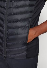 Black insulated jacket featuring quilted texture on the front, side zipper pocket, and smooth fabric on the back with a fitted design.