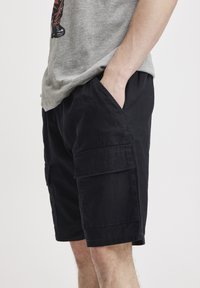 Zwarte cargoshorts met twee zijzakken, gemaakt van lichtgewicht stof, met een relaxed fit en een knie-lange snit. Textuur is zichtbaar.