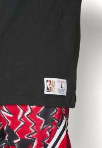 Maglia NBA nera con etichetta bianca che riporta "HWC" e taglia "L", abbinata a pantaloni corti da basket con motivo zigzag rosso, nero e bianco.