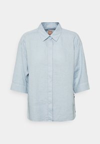 Ljust blå skjorta med knappar tillverkad av linne. Har en spetsig krage, korta ärmar och en rak passform med sidofickor.