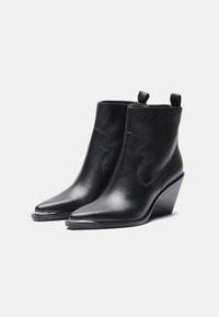 Bottines en cuir noir avec des pointes aigües, des accents cousus et un talon compensé. Présente une surface lisse et des languettes à l'arrière pour un enfilage facile.