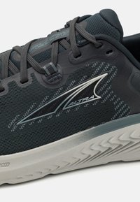 Scarpa sportiva con tomaia in mesh grigio scuro, logo riflettente argento, suola grigia con texture e design dei lacci intricati per una calzata sicura.