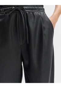 Czarne spodnie z faux skórki z elastycznym paskiem, bocznymi kieszeniami oraz gładką fakturą, podkreślające luźny krój i nowoczesny design.