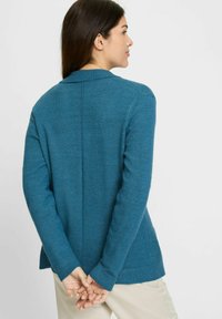 Cyanfarbener Cardigan aus strukturiertem Strickstoff, mit einem dezenten Kragen, langen Ärmeln und seitlichen Schlitzen, einem geraden Rückennaht und gerippten Bündchen.