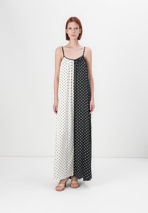 Maxi dress with a dual color scheme: white with black polka dots on one side and solid black on the other. Thin spaghetti straps.