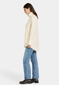 Creme fleece pullover med høj krave, lange ærmer, en afslappet pasform og sideslidser, parret med lyseblå lige ben jeans og sorte støvler.