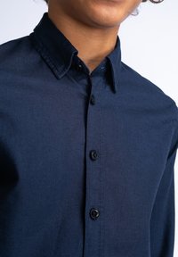 Camicia blu navy con tessuto strutturato, dotata di colletto classico e bottoni neri. Vista ravvicinata della parte frontale.