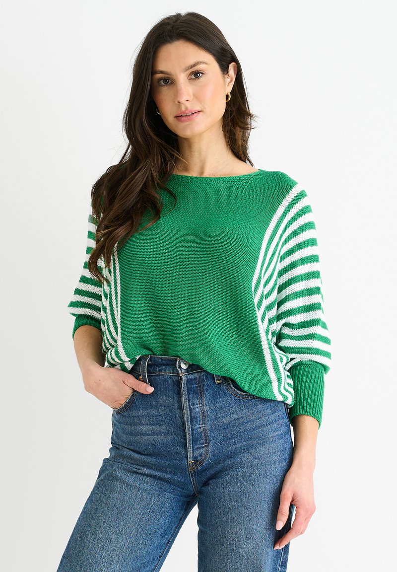 Grüner gestrickter Pullover mit weißen Streifen an den Ärmeln, entspannter Schnitt, runder Halsausschnitt und strukturierter Stoff, kombiniert mit hochgeschnittenen Jeans.