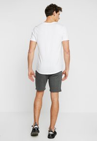 Maglietta bianca a girocollo abbinata a pantaloni corti grigio scuro. La maglietta ha un design semplice e i pantaloni sono realizzati in un materiale morbido e elastico.
