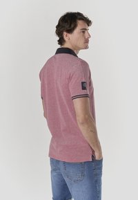 Punane kirju polo-särk tumesinise krae ja mansettidega; vasakul varrukal väike logopatch ja lõdva lõikega disain.