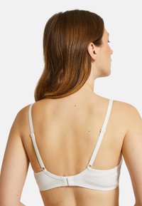 Soutien-gorge blanc avec de fines bretelles réglables, doté d'une fermeture croisée à l'arrière et de détails de couture subtils le long des bords.