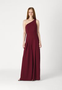 Combinaison bordeaux à une épaule en tissu doux. Présente un buste ajusté, des jambes larges plissées et un design minimaliste.