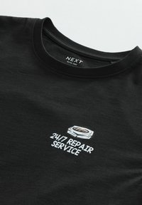 Musta puuvillane T-särk ümarate kraega. Omab graafilist printi logoga ja tekstiga "24/7 REPAIR SERVICE" valgel taustal. Pehme tekstuur.