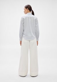 Cămașă cu dungi albastre și albe, cu mâneci lungi și manșete cu nasturi, asortată cu pantaloni albi evazați, cu tiv pliat.