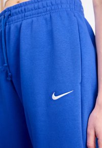 Blaue Sweatpants aus weichem Stoff mit einem elastischen Bund und einem weißen Nike-Logo an der Seite. Enthält eine verstellbare Kordel.