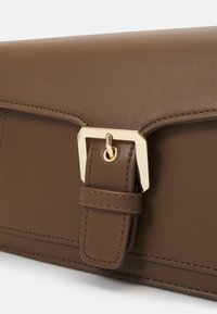 Brown leather bag with a gold metallic buckle and strap. Smooth texture, square shape, and visible stitching along the edges.