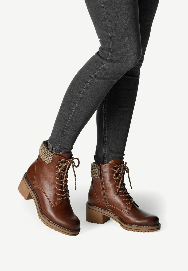 Bottes en cuir marron à mi-mollet avec un col en tricot texturé, un laçage à l'avant et un talon épais. Associées à un jean skinny en denim foncé.