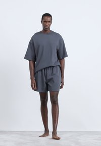 Tricou din bumbac gri, cu mânecă scurtă, asociat cu pantaloni scurți asortați. Ambele au un croi lejer, cu o textură netedă și un design minim.