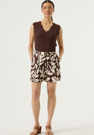 Top senza maniche bordeaux con tessuto strutturato, abbinato a pantaloncini crema con motivo a foglie. Presenta tasche e vestibilità rilassata, indossato con sandali con tacco marroni.