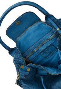 Struktureret blå læderhåndtaske med en glat indvendig del, lynlåskompartementer og detaljer i messing. Indersiden har et logo-patch.