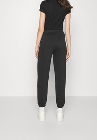 Černé bavlněné tepláky s elastickým pasem a stahovacími lemy na kotnících, doplněné přiléhavým černým tričkem a bílými teniskami.