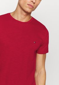 T-shirt rossa in cotone con maniche corte, colletto a girocollo e un piccolo logo sul petto. Tessuto liscio, design leggero.