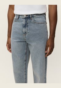 Light blue denim jeans with a relaxed fit, featuring a five-pocket design, button closure, and subtle fading along the thighs.