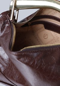 Brun läderväska med en guldlampa, en zippered inre ficka och en texturerad yta. Insidan är klädd med märkesväv.