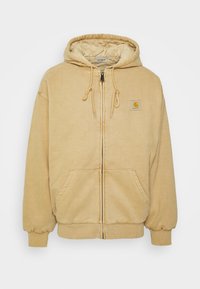 Sudadera con cremallera en color beige, hecha de una tela suave, con un bolsillo cosido, capucha con cordón y puños elásticos. Diseño sencillo con mínima marca.