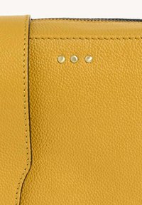 Cuir jaune texturé avec une finition lisse, présentant trois petites clous dorés près du bord et une couture contrastée.