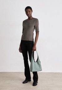 Brown ribbed short-sleeve top, black flared pants, black ankle boots, and a green leather bag with a curved design and contrasting black accents.
