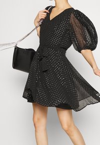 Black dress with puff sleeves, cinched waist, and a V-neck. The fabric features a pattern of metallic dots. Includes a tied belt and a small black bag.
