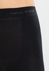 Čierne elastické spodné prádlo s mäkkým elastickým pásom, na ktorom je v šedej farbe logo "Calvin Klein". Hladká textúra, stredne vysoký strih.