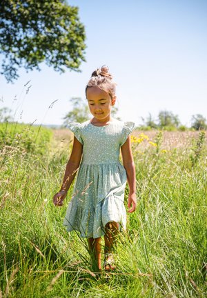Grünes Kleid mit blumigem Muster, kurzen Rüscheärmeln und geschichtetem Rock. Der Stoff wirkt leicht und atmungsaktiv, ideal für warmes Wetter.
