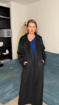 Cappotto di lana nero con design doppiopetto, ampi revers e tasche laterali, indossato sopra un maglione blu lavorato a maglia.