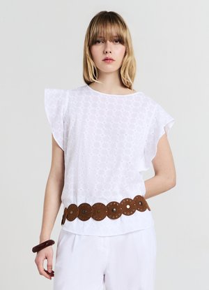Haut blanc en broderie anglaise avec manches volantées, tissu texturé, et ceinture ronde en cuir marron ornée de découpes circulaires et de clous, porté par un mannequin.